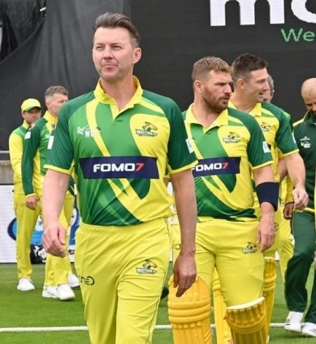 Australia Champions cricket squad walking onto field in green and yellow kits showing FOMO7 principal partner logo.